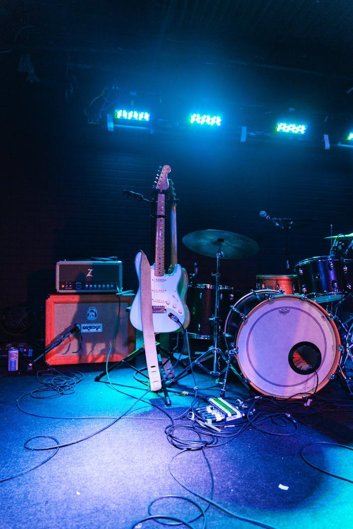 Electric guitar and drum set on an illuminated live music stage, ready for performance.